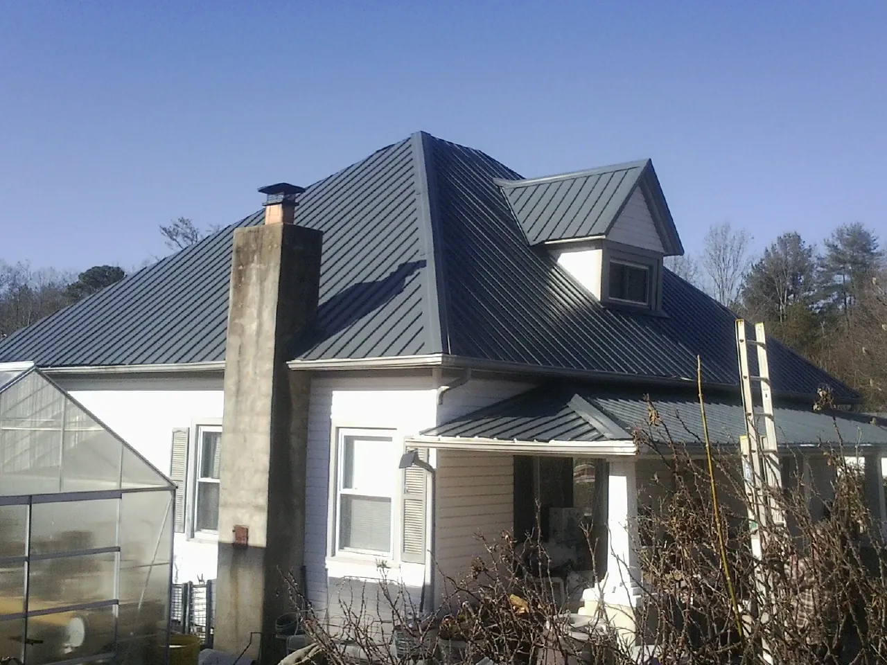 Dark blue standing seam metal roof on a white farmhouse with dormer — Slate & Tile Roof Repair by Roofing Brothers in Stites