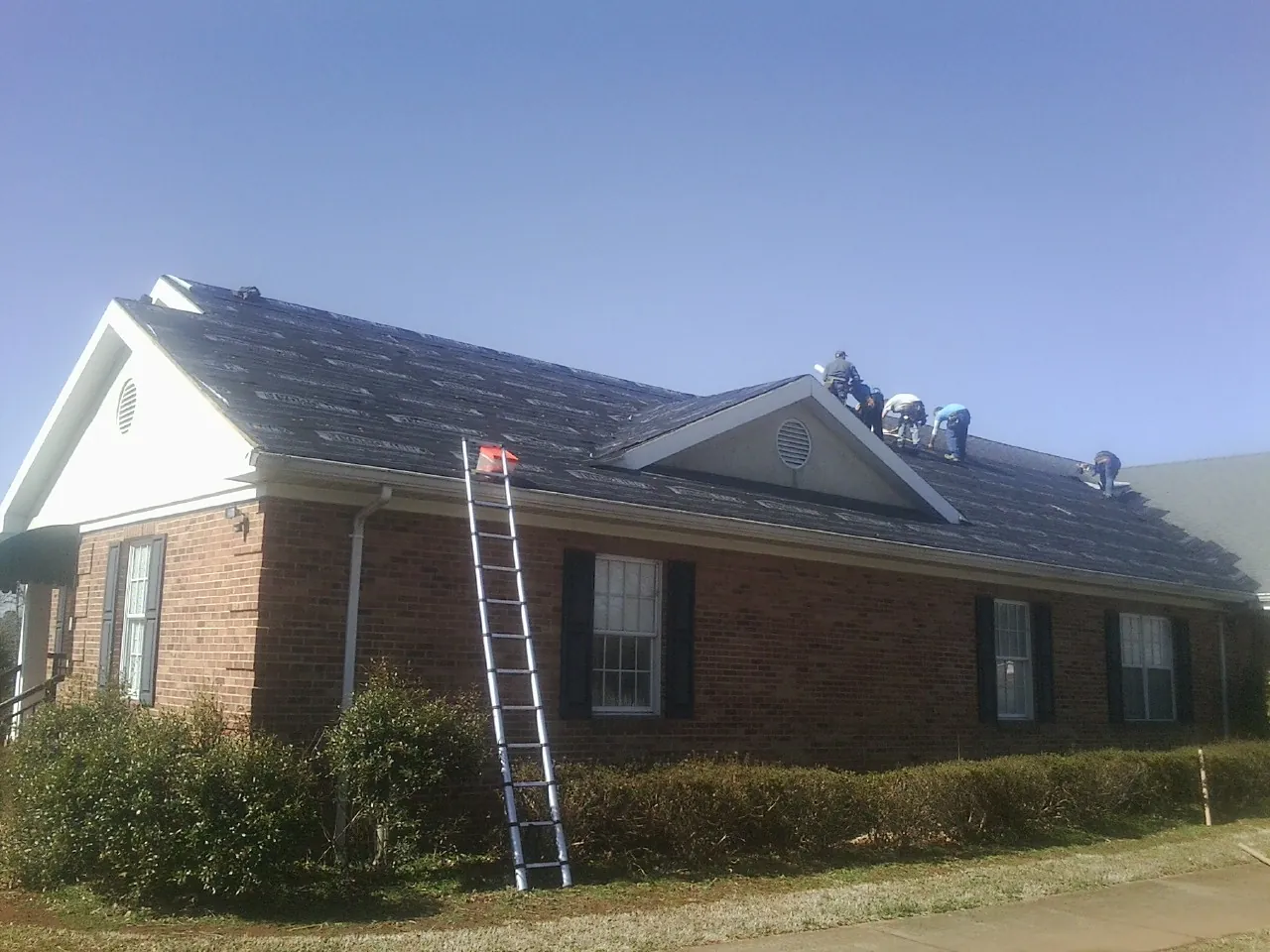 Crew tearing shingles off a brick ranch roof with a ladder set — Emergency Roof Repair work by our crew in Stites