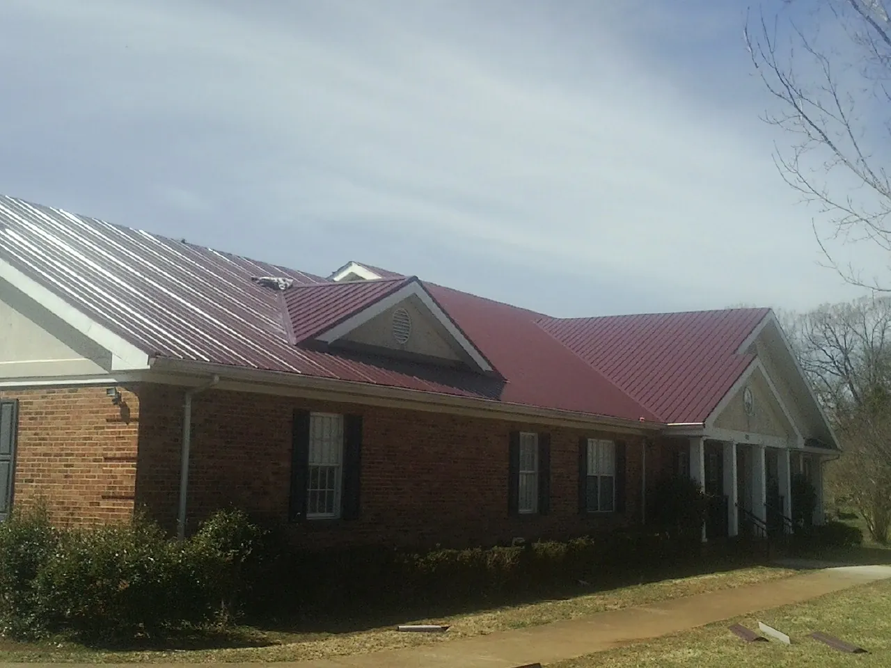 Red metal roof with gabled entries on a long brick building, from a Hail Damage Roof Repair job in Stites