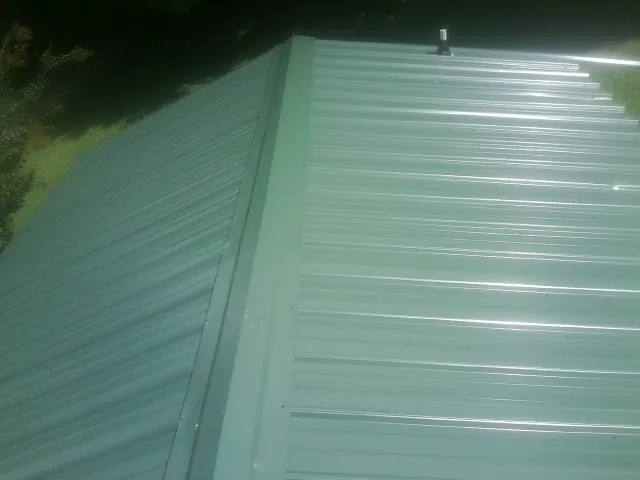 New green metal panels meeting at the ridge of a roof — Flat Roof Repair work by our crew in Stites