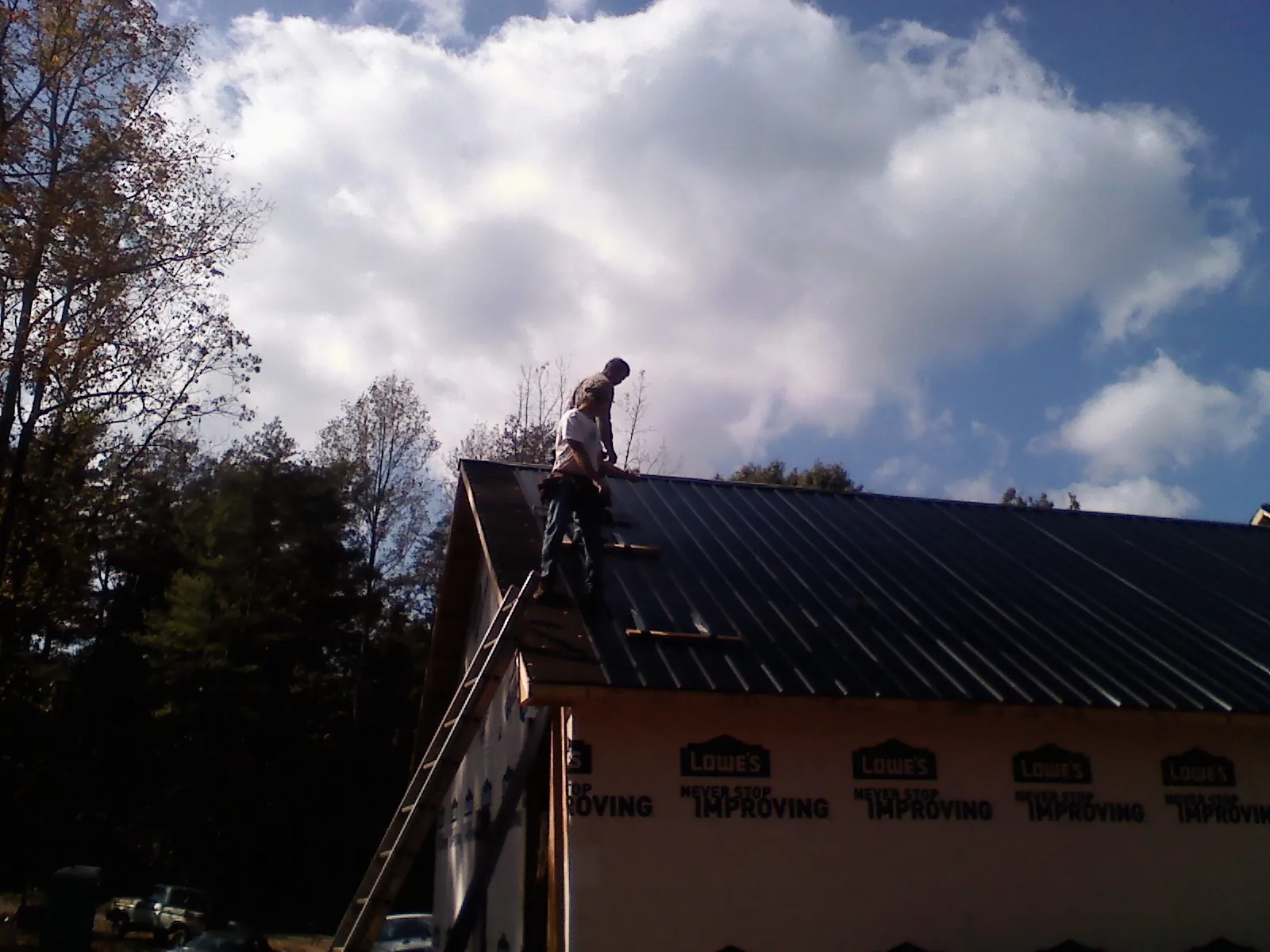Roofer fastening dark metal panels high against a cloudy sky, from a Roof Inspection job in Stites